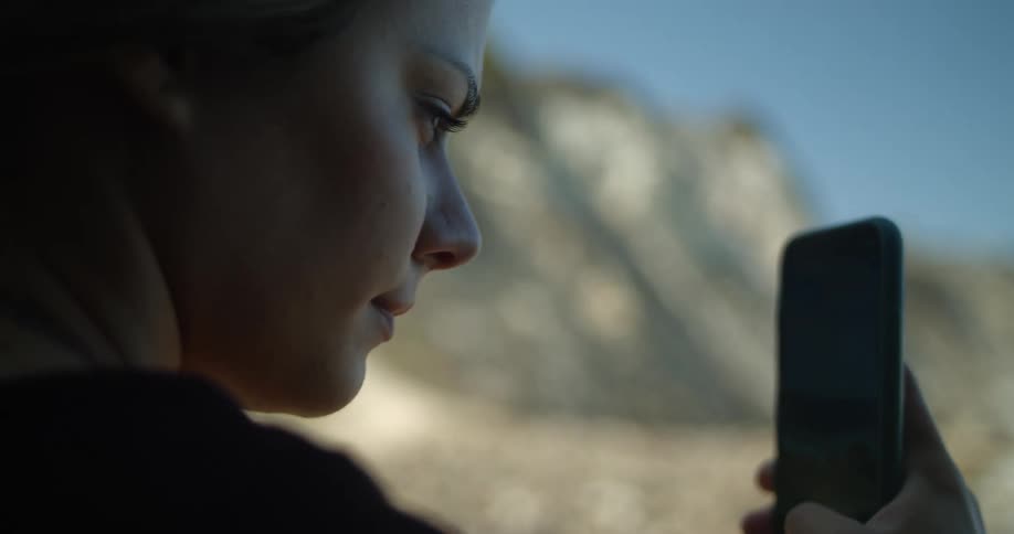 A teenage girl uses her cell phone to takes pictures of the hilly terrain that she is at the bottom of