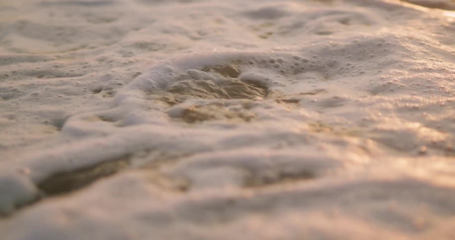 A small wave washes upon a sandy beach and flows over smooth rocks
