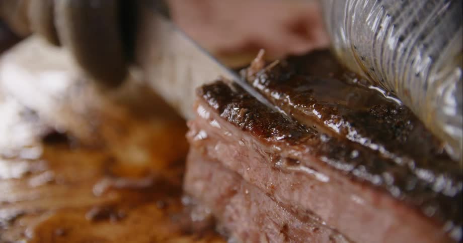 A person with a glove cutting a piece of meat with a knife on a cutting board