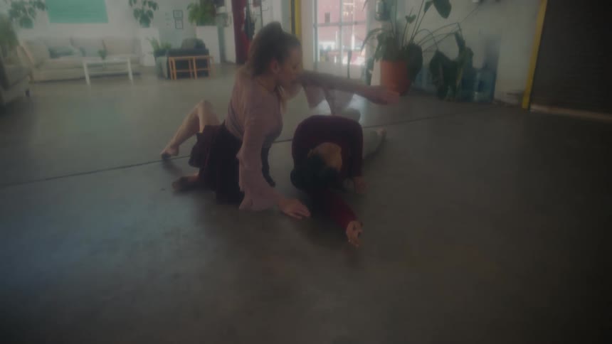 Two young women roll on the floor together as they perform a modern dance in a loft apartment