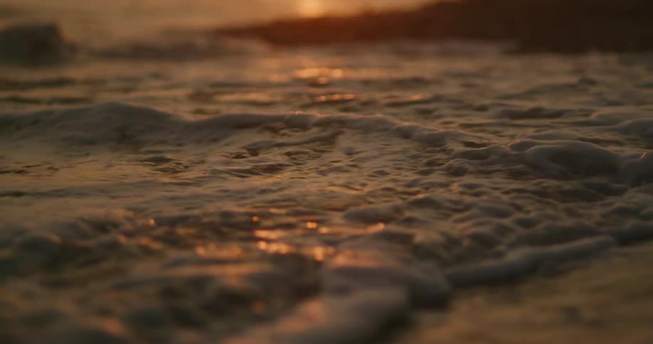 Golden sun shines and shimmers on waves coming to shore covering the sand and stones