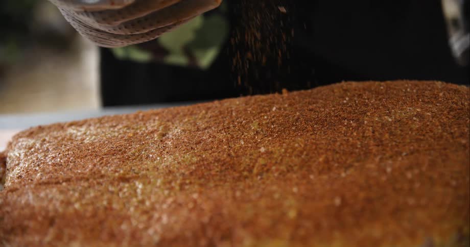A person with gloves sprinkling seasoning on a piece of meat on a cutting board on a table