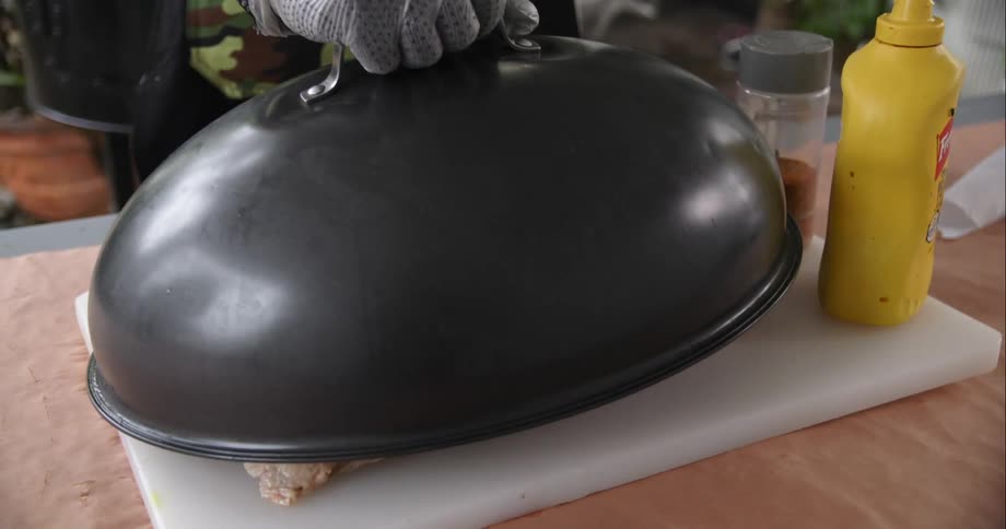 A person with gloves removing a lid with a piece of meat and a cutting board underneath