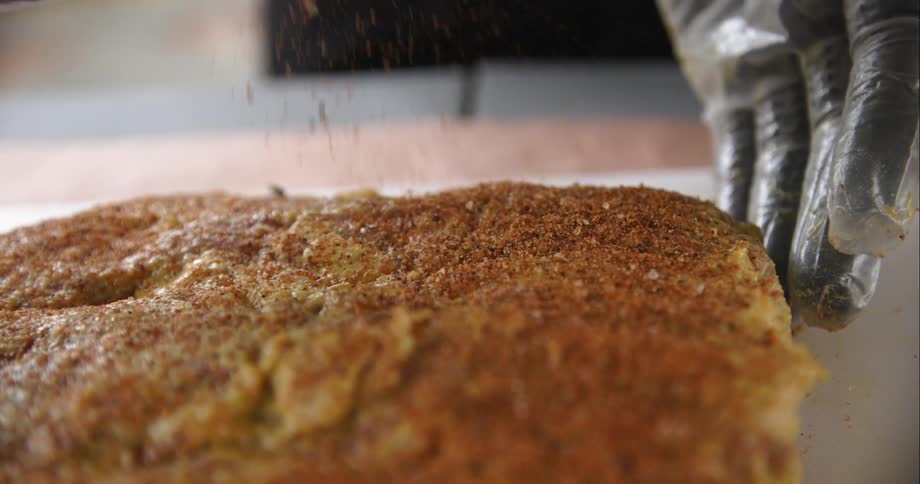 A person wearing gloves carefully sprinkled seasoning atop a large slab of meat