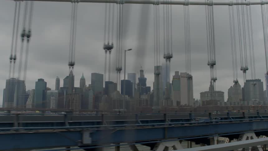 Moving over the very top of a large bridge with a city in the distance