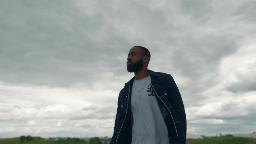 Man walks across field under overcast sky with buildings in background