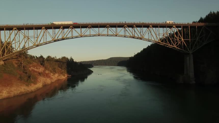 A river flows through a wooded area and under an expansion bridge