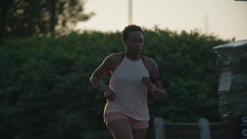 Woman uses arm mobile phone holder while jogging past hedges