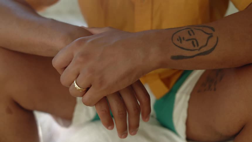 Tattoo on the forearm of a man wearing shorts and yellow shirt sitting outdoors