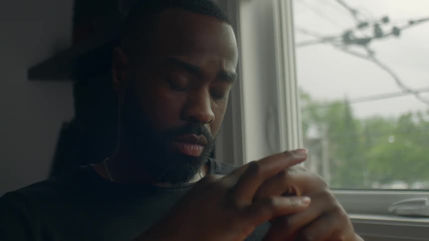 Young bearded man praying or thinking while looking out the window at home