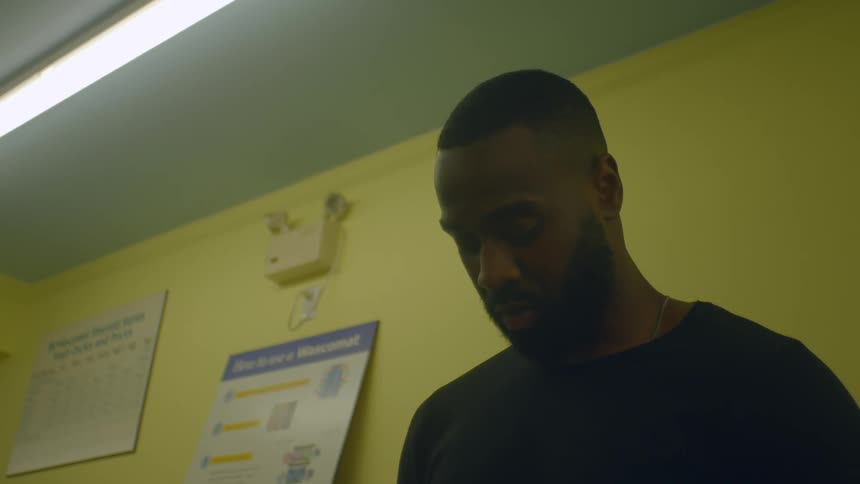 A man in a shirt in a room with signs and a wall in the background