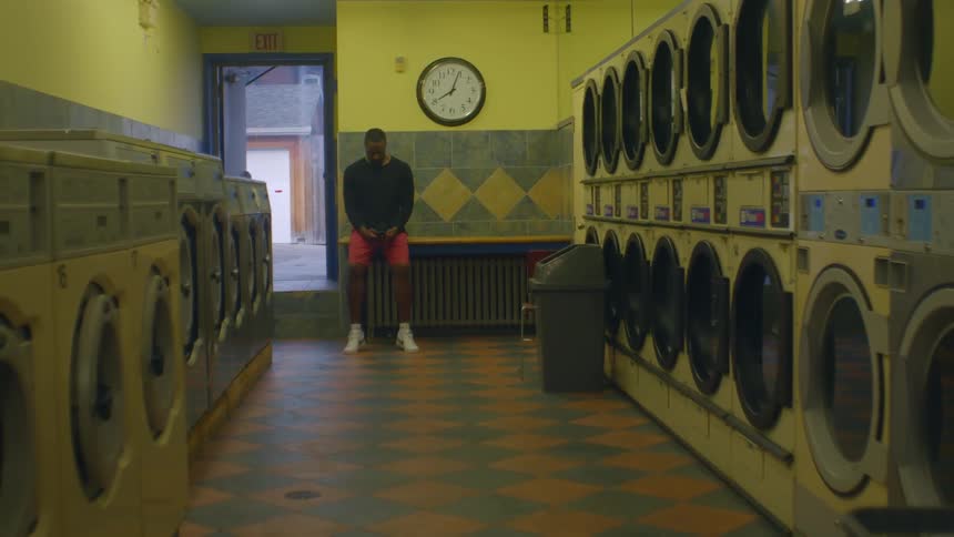 Man with a black sweater and red shorts sits on bench in laundry room