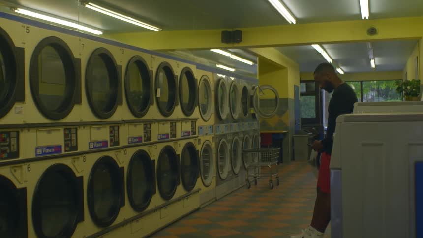 Young man looking at his phone while waiting on the laundromat at evening