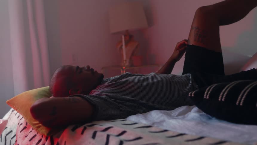 A mans kitten joins him in bed as he relaxes with a leg against the wall