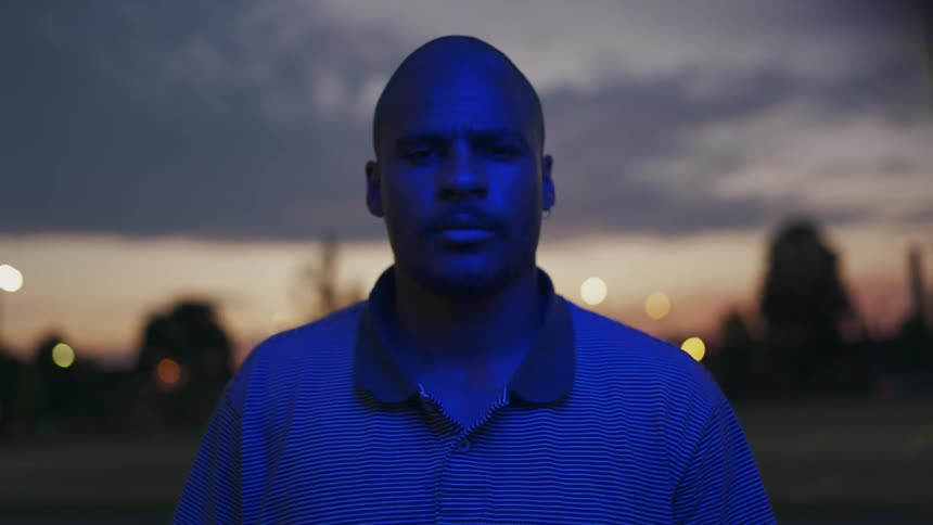 A man standing outside at sunset with emergency red and blue lights flashing over him