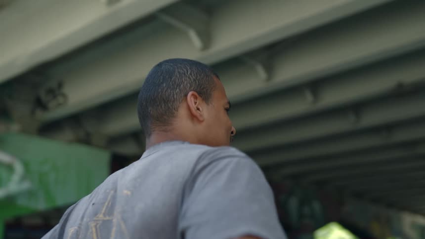 A man standing underneath an overpass with trees the sky and clouds in the background