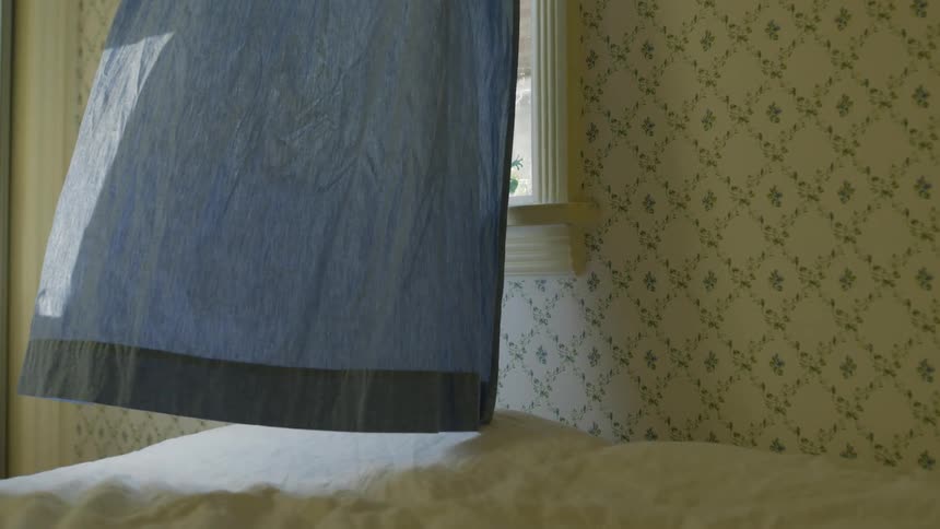 A blue curtain over an open bedroom window billows in the breeze