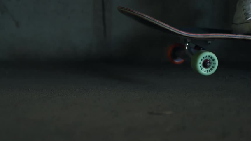 Skateboarder wearing sneakers bounces skateboard up and down against concrete