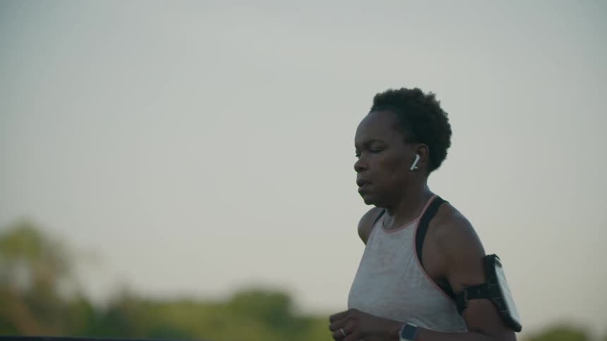 A woman runs along a bridge while using wire earbuds and her smartphone