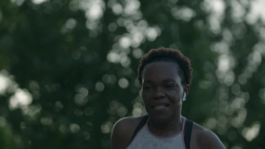 A young woman with airpods in and her cell phone in an armband smiles as she runs