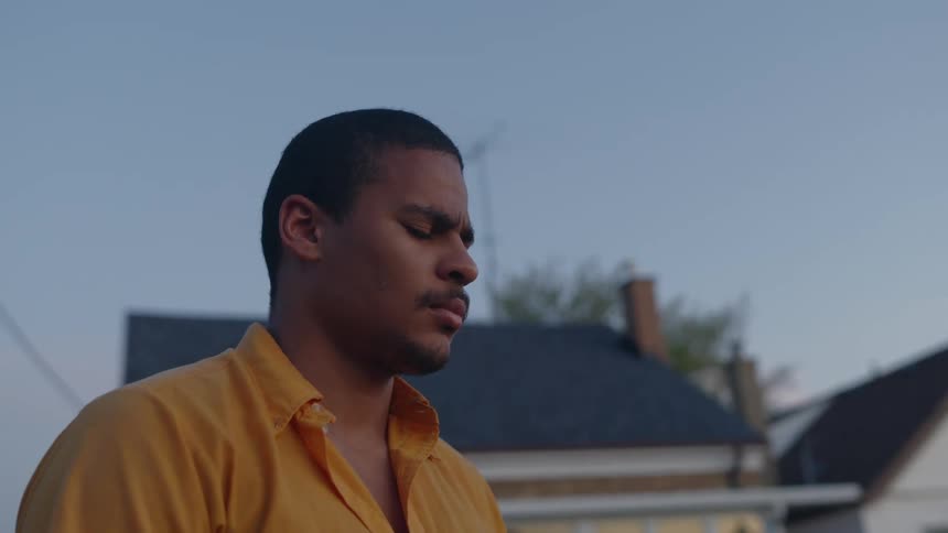 Young man wearing yellow shirt stands on the neighborhood street with his eyes closed at morning