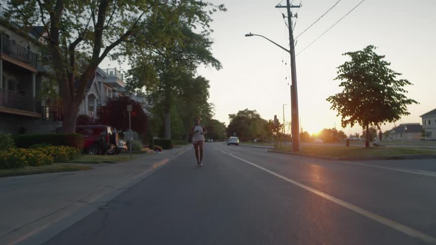 A woman jogs along a residential street as the sun sits very low in the sky