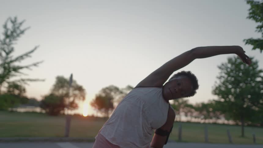 A woman in athletic wear does stretches in a parking lot in the evening