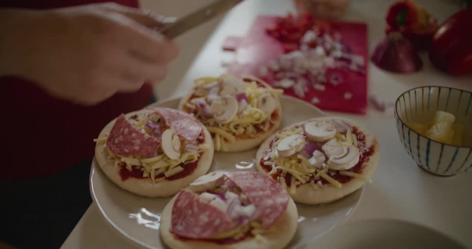 A man cuts meat as he assembles pizzas