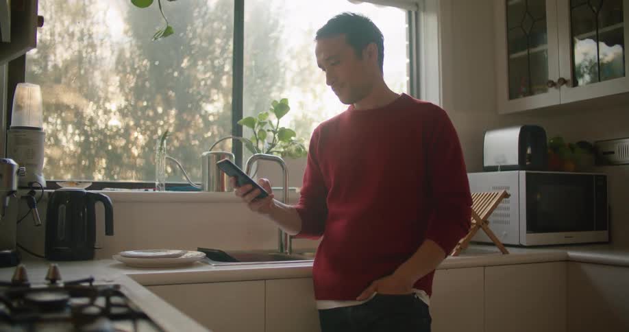 A man is using his cellphone in the kitchen
