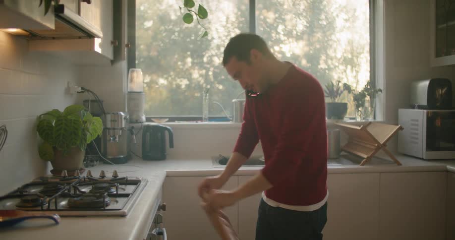 A man cleans up his kitchen while talking on the phone