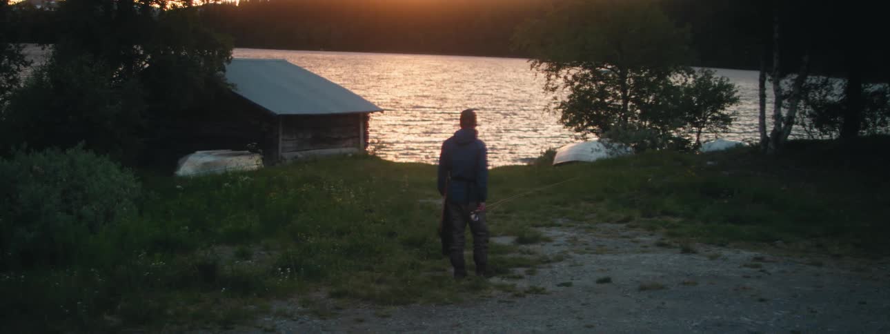 A man stands on the shore holding a fishing rod and looking out at the water