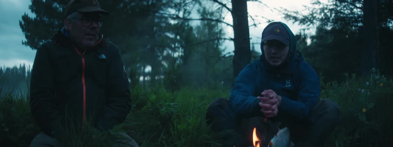 Couple of friends sitting on the forest in front of a campfire at morning