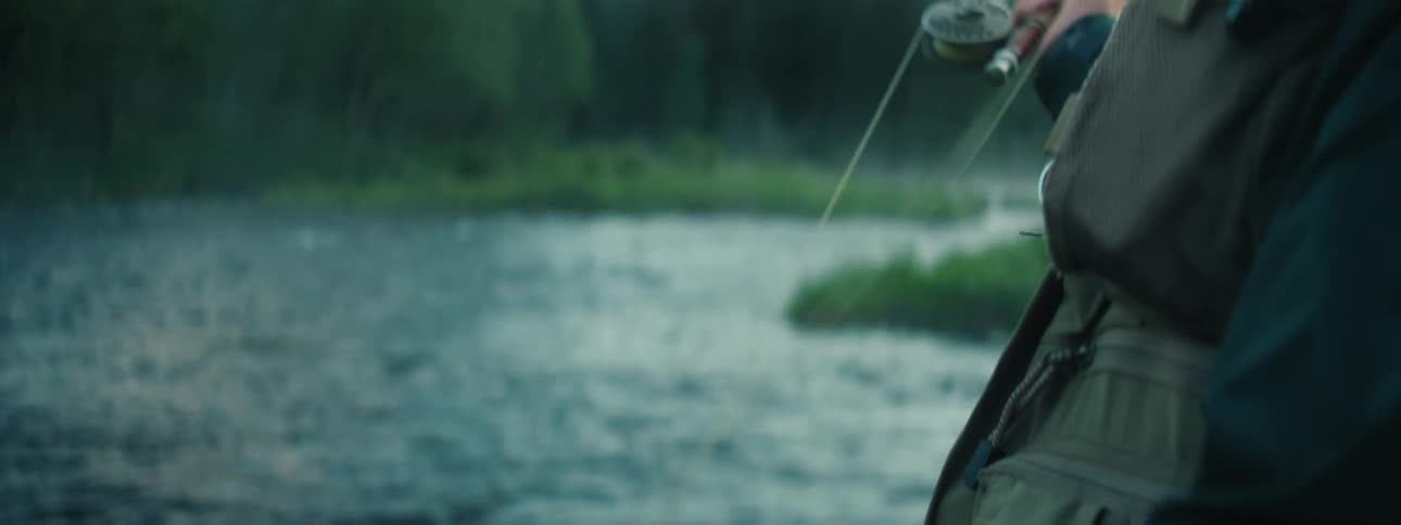 A man standing in a river is fishing in the early morning