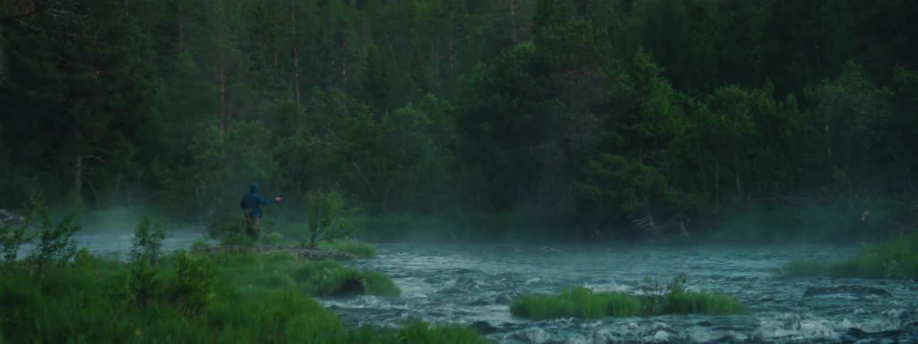 A person fishing in a river with a fishing rod with trees the sky and clouds in the background
