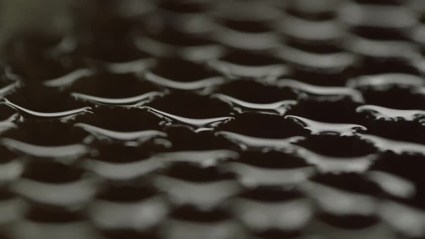 Oil coats the surface of and drips through the holes of a metal grate