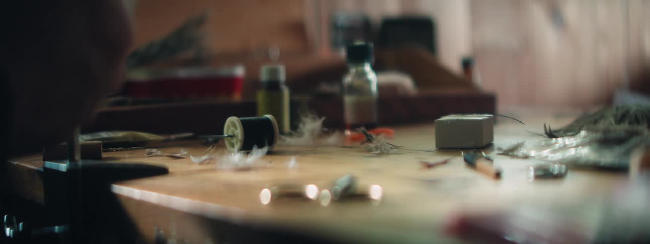 A person sitting at a work table picks up and puts down various supplies and tools as they are putting something together
