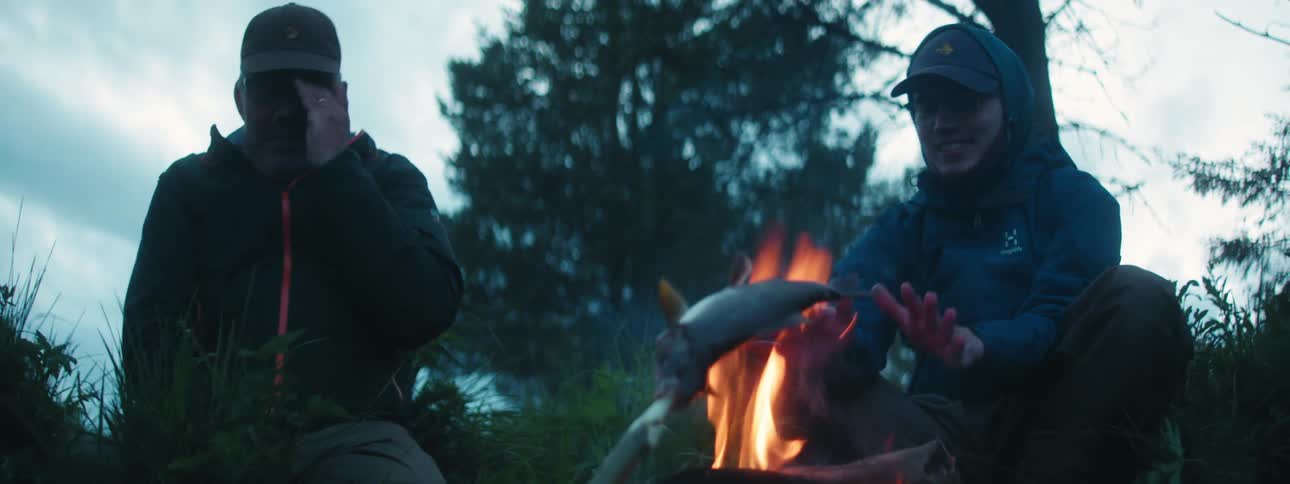 Two men in raincoats warming up at a campfire