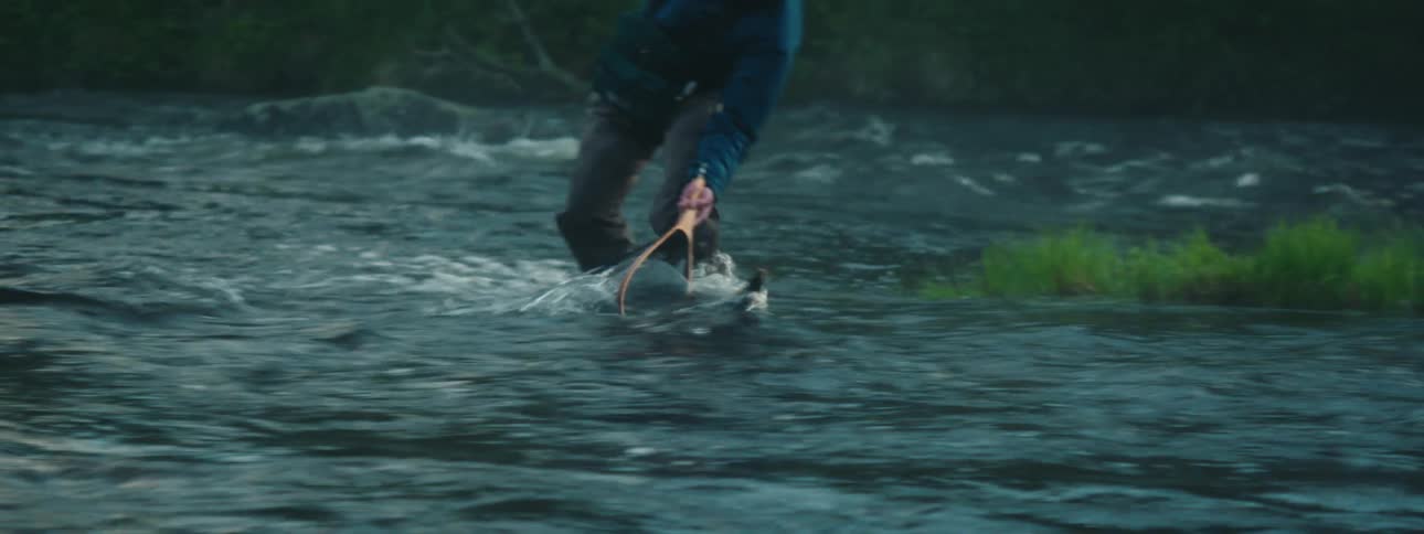 A man catches a fish and puts it in his net on the stream