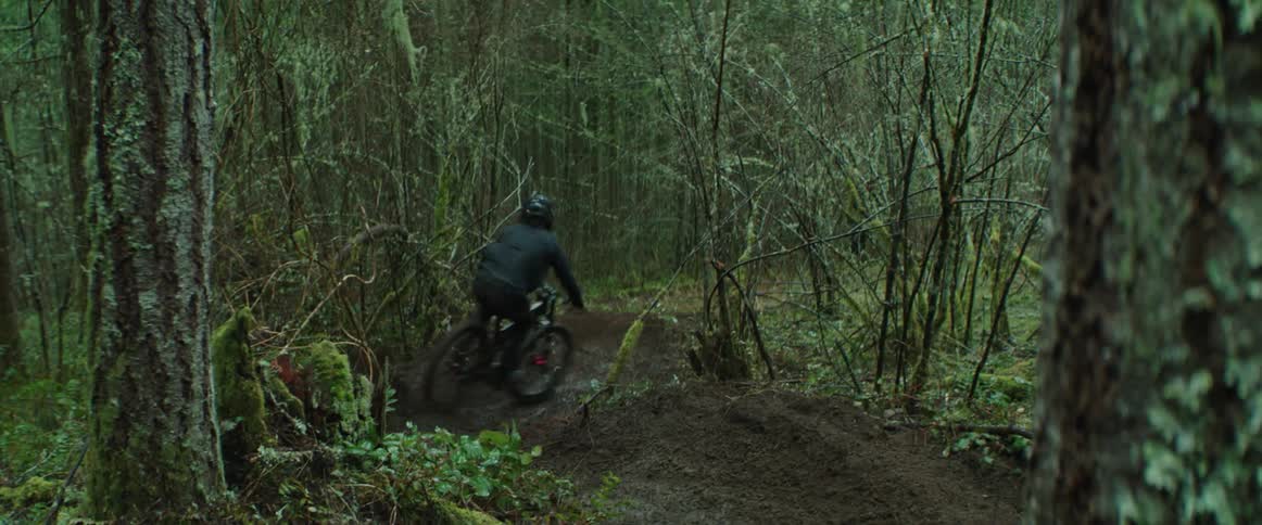 A man carves his mountain bike through sharp, muddy corners in the woods