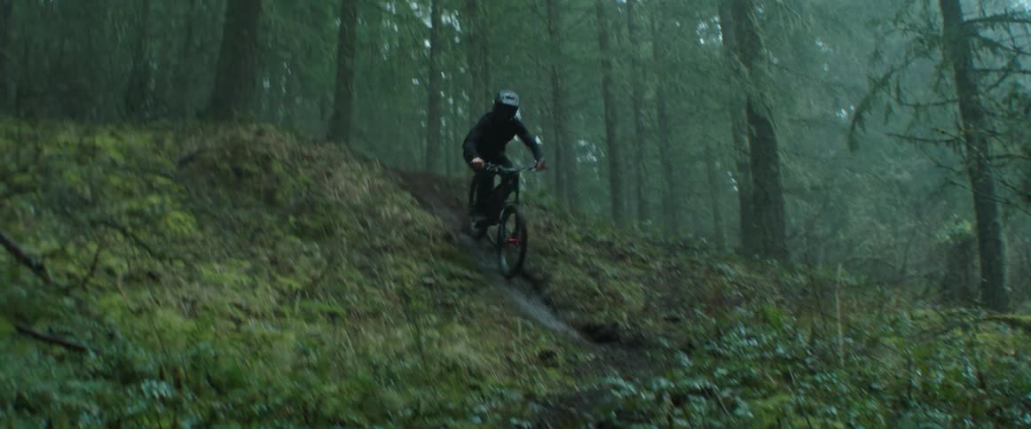 A person on a mountain bike carves down a wet rock roll and corner in foggy forest