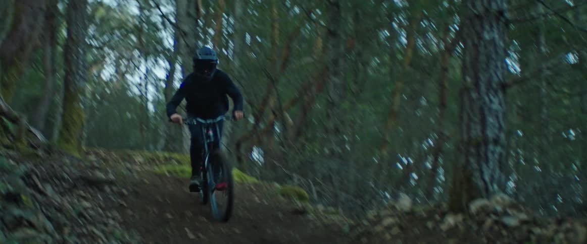 A mountain biker lands a jump and immediately hits fast corner on trail