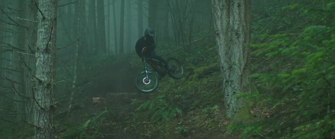 A mountain biker whips his bike sideways after hitting dirt jump on foggy forest trail