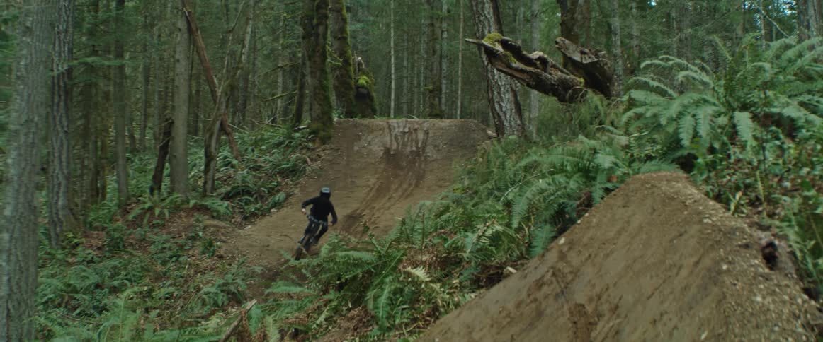 A mountain bike rider hits a sequences of jumps riding through a fast custom trail in the forest