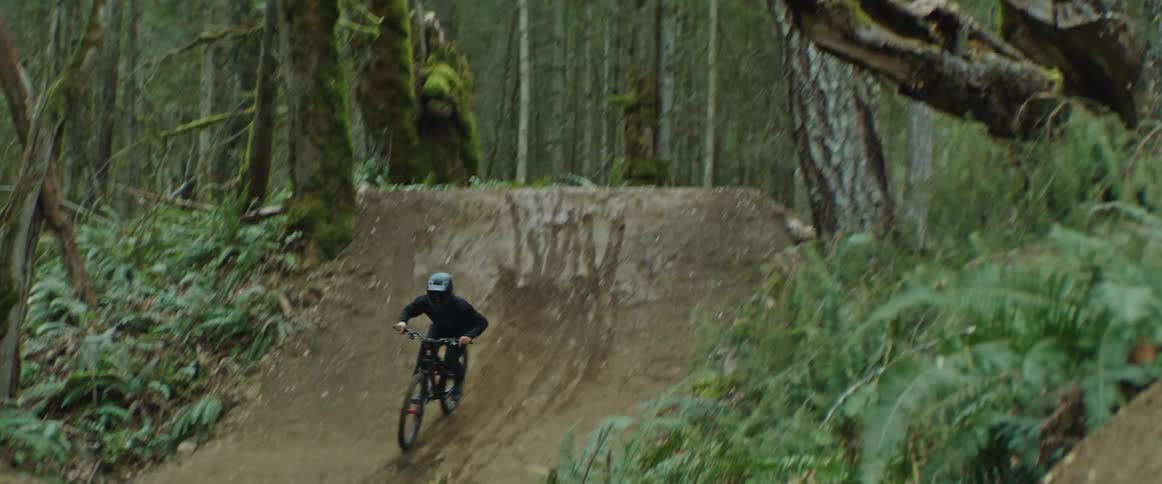 A mountain bike rider hits a jump on a dirt trail in the woods