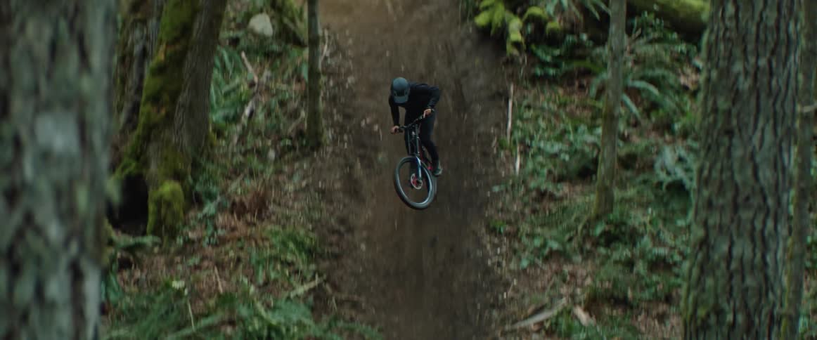 A man stylishly manoeuvers his mountain bike through a sweeping dirt trail feature in the forest