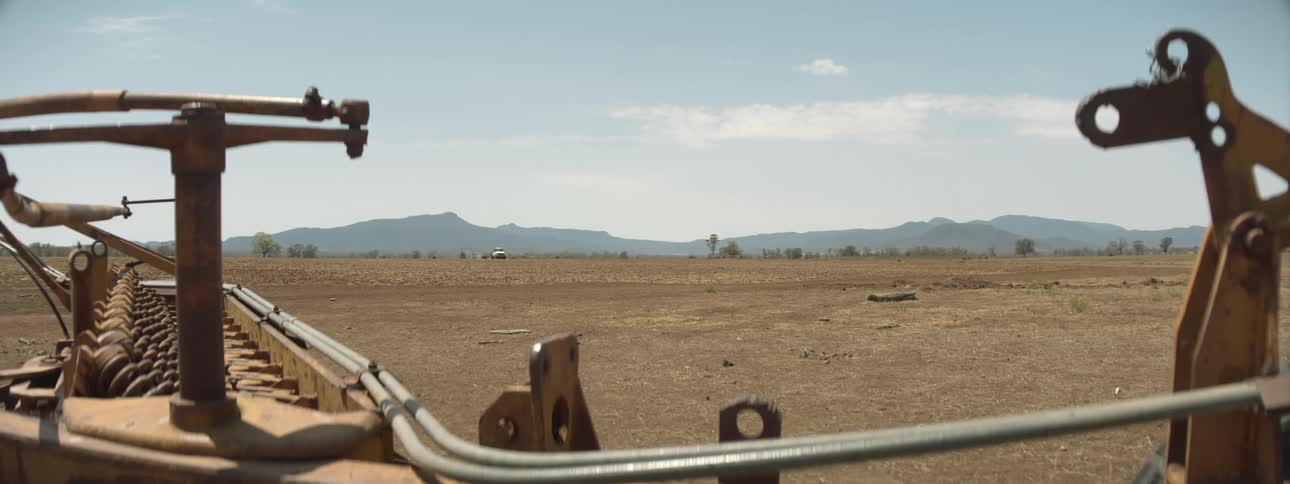 A white pickup truck travels over barren land near farm equipment