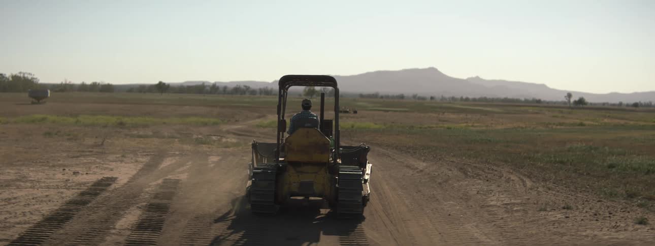 A man drives a bulldozer through an open field