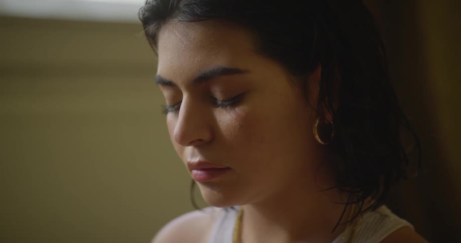Women leans against wall near window with eyes closed lowering her head