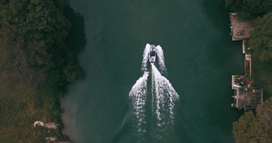 A boat pulling someone on a wakeboard along a river