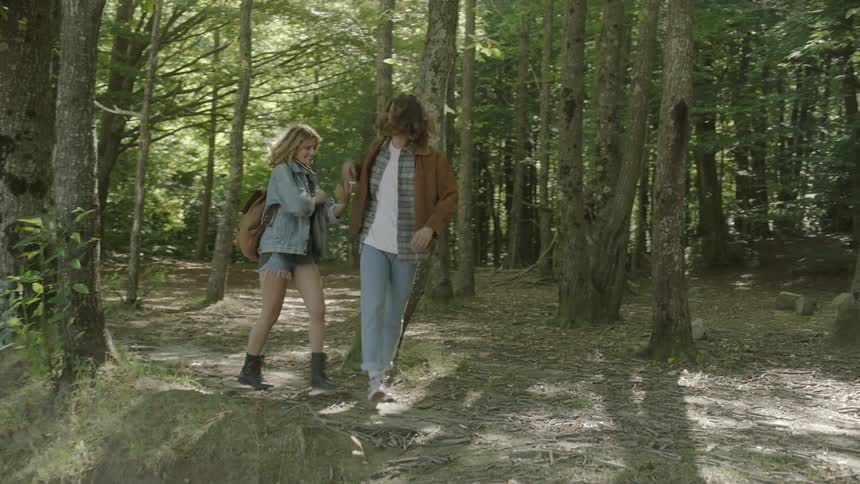 A man and woman play fight and laugh while walking through a forest